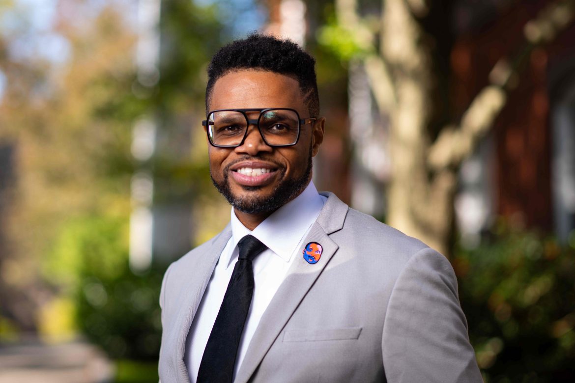 Headshot of Monroe France wearing black tie and grey blazer jacket with a custom MLK lapel pin